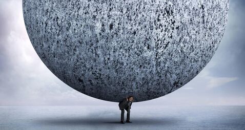 Businessman Bending Over To Support Very Large Stone Sphere On His Back