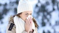 Woman blowing in a tissue in a cold winter with a snowy mountain in the background