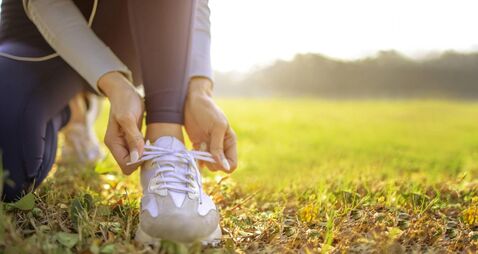 iStock-1298108434.jpg young woman runner tying her shoes preparing for a jog outside at morning