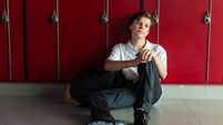 Teen student sitting by red lockers, wearing casual clothes.