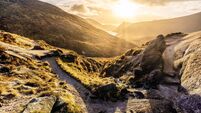 Footpath and large boulder leading to valley with water reservoir, dramatic sunset with sunrays. Mourne Mountains