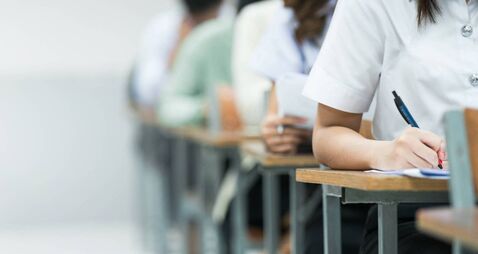 Students Taking Exam in Classroom Setting. Students in uniforms are seated in a classroom, writing answers during an exam, highl