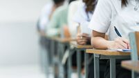 Students Taking Exam in Classroom Setting. Students in uniforms are seated in a classroom, writing answers during an exam, highl
