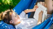 Cute girl reading a book in a hammock in the garden.