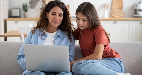 Young mother and teen girl daughter sitting on sofa using laptop planning vacation
