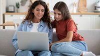 Young mother and teen girl daughter sitting on sofa using laptop planning vacation