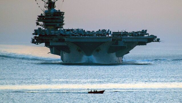 <p>A small vessel transiting in front of the aircraft carrier USS George HW Bush as it transits the Strait of Hormuz in 2014. Picture: AP Photo/US Navy, Specialist 3rd Class Abe McNatt</p>