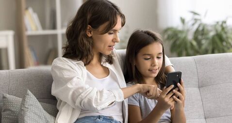 Engaged mom showing cute child girl how to use application